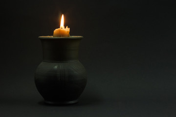 Burning candle in a black ceramic pot on a dark background. Concept of divination, magic, ritual. Copy space.