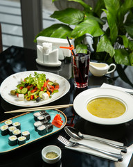 lunch setup with vegetable soup, nori sushi set, greek salad and chery juice
