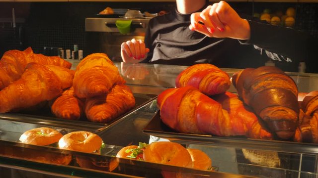 Girl barista puts a croissant layout tray on glass showcase in a cafe