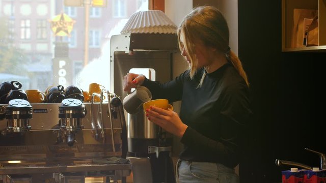 Cute young barista girl in cafe makes coffee cappuccino latte art drawing with milk in the morning