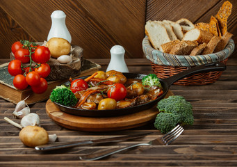 roasted beef in sauce with potatoes, tomatoes, broccoli, carrots in cast iron pan