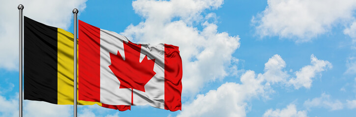 Belgium and Canada flag waving in the wind against white cloudy blue sky together. Diplomacy concept, international relations.