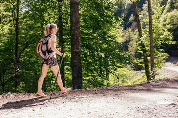 Side view of a young slim girl in sportswear is engaged in trekking in the mountains with sticks for sports walking. Fitness and tourism concept
