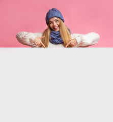 Blonde girl in winter hat pointing at blank white board