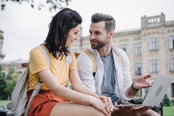 happy young woman sitting near bearded man using laptop