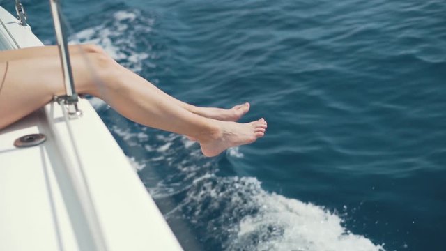 Female legs hanging from the yacht. The yacht moves along the waves. Girl enjoys the journey