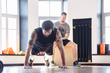 Two friends men in good physical shape doing workout together in the gym. Concept of team spirit...