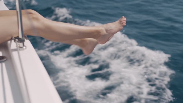 Female legs hanging from the yacht. The yacht moves along the waves. Girl enjoys the journey