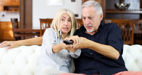 Mature couple fighting for remote control on a sofa