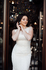 Smiling cheerful girl enjoys freedom, standing next to door. Portrait of adorable young woman in white dress.  Beautiful woman with professional make up  and manicured nails. 