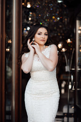 Smiling cheerful girl enjoys freedom, standing next to door. Portrait of adorable young woman in white dress.  Beautiful woman with professional make up  and manicured nails. 