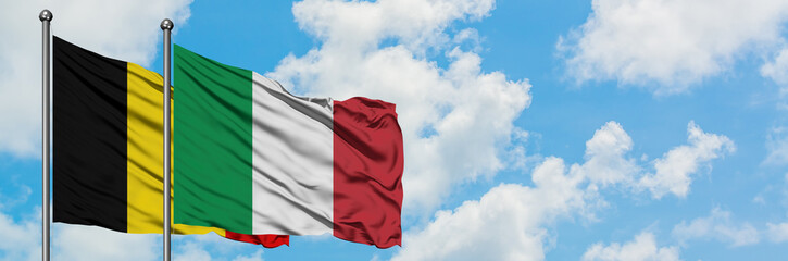 Obraz premium Belgium and Italy flag waving in the wind against white cloudy blue sky together. Diplomacy concept, international relations.
