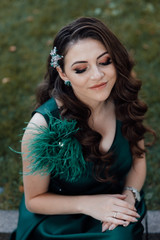 Young pretty lady in green dress. Fashion photo. Beautiful long curly hair woman with closed makeup eyes and manicured nails.  Young beautiful stylish girl posing.  Female fashion.