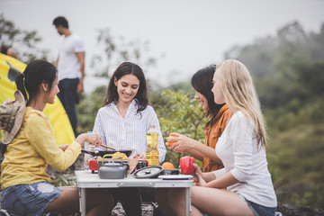 Camping concept - Group of friends were sitting and enjoying cooking together, with kitchen equipment lined up on the table.