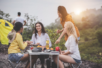 Camping concept - Group of friends were sitting and enjoying cooking together, with kitchen equipment lined up on the table.