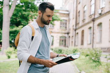 Handsome bearded tourist holding map near building