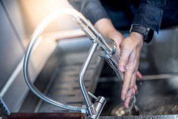 Washing hand in kitchen sink with modern stainless faucet. Saving water concept