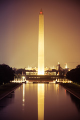 The Washington Monument at night with its image reflected in the National Mall reflecting pool.