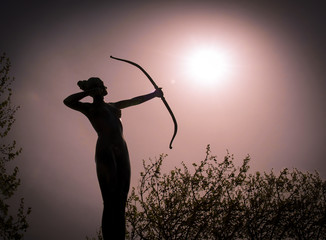 Statue of a woman Archer Silhouette with a bow target the sun