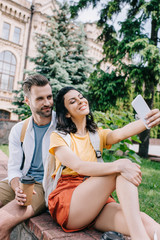 Happy woman talking selfie with handsome man near building