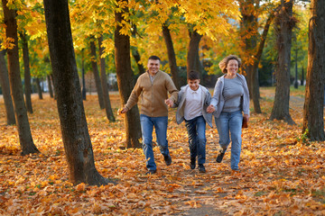 Obraz premium Happy family having holiday in autumn city park. Children and parents running, smiling, playing and having fun. Bright yellow trees and leaves