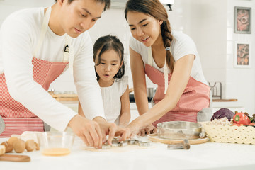 Obraz na płótnie Canvas Young asian family cooking food in kitchen.Happy Little girl with her father and mother mixing batter.mother and Little girl preparing the dough.Happy family in the kitchen and junior chef Concept.