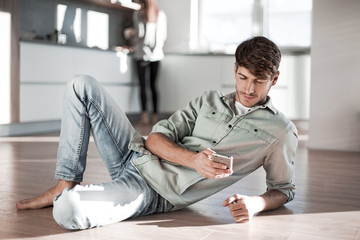 young man with smartphone sitting on kitchen floor