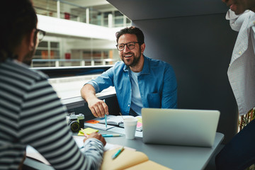 Three laughing designers working in an office meeting pod