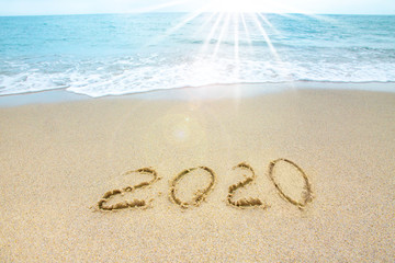 New Year 2019 on the sandy shore against the backdrop of sea waves. Beautiful sunrays illuminate the inscription 2020 on the sand.
