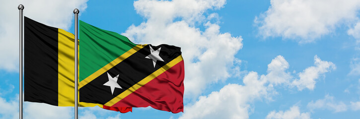 Belgium and Saint Kitts And Nevis flag waving in the wind against white cloudy blue sky together. Diplomacy concept, international relations.
