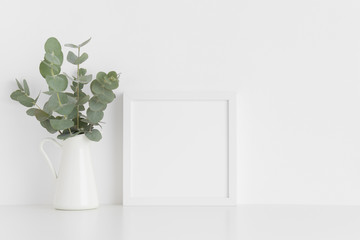 White square frame mockup with a bouquet of eucalyptus in a vase on a white table.Portrait orientation.
