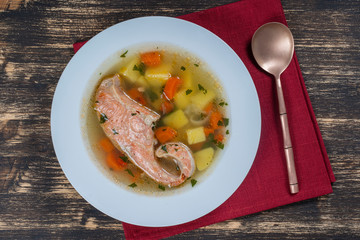 Fresh salmon fish soup with carrots and potatoes in a white plate, close up