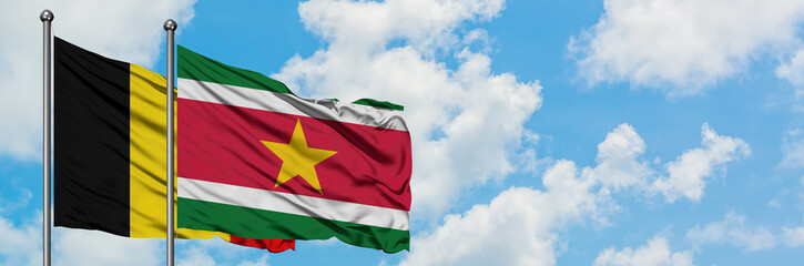 Obraz premium Belgium and Suriname flag waving in the wind against white cloudy blue sky together. Diplomacy concept, international relations.