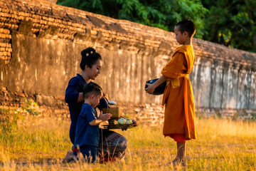 Monk Buddhist elder Novice. The family Children woman putting food offerings in a monk's alms bowl and a woman prostrating oneself to respect worship monks, monks walking routine every morning.