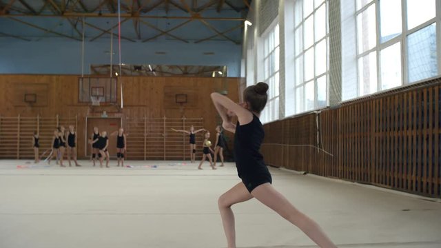 Side view of young teenage or primary school girl doing standing split and practicing rhythmic gymnastics dance movements