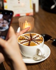 woman taking photo of cappuccino with her smartphone