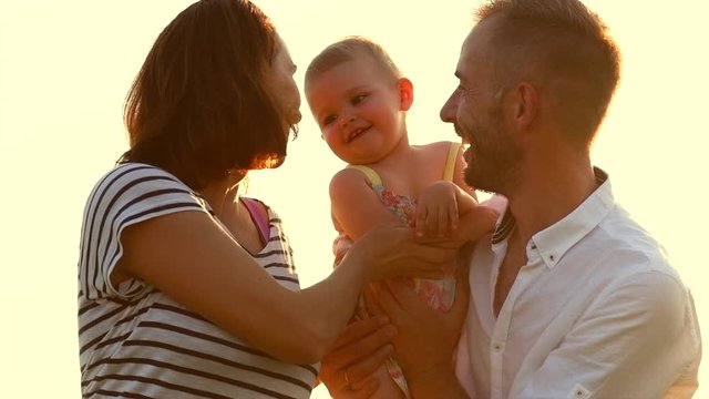 Happy joyful young family with child. Father, mother and little girl having fun outdoors, playing together in summer field, countryside. Mom, Dad, baby laughing, hugging, enjoying nature Slow motion