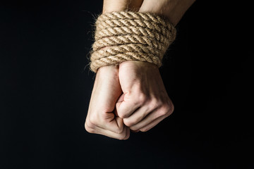 hands tied with rope on black background