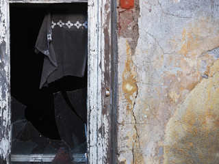 Destruction and desolation, a fragment of an abandoned house, a broken window, torn curtains