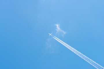 Airplane in a blue sky with clouds and condensation trails, Germany