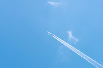 Airplane in a blue sky with clouds and condensation trails, Germany