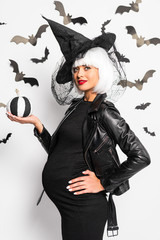 pregnant woman in witch hat and wig holding pumpkin in Halloween