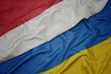 waving colorful flag of ukraine and national flag of indonesia.
