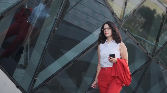 Confident business woman in a strict red suit uses a smartphone on the go