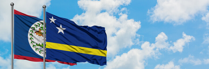 Belize and Curacao flag waving in the wind against white cloudy blue sky together. Diplomacy concept, international relations.