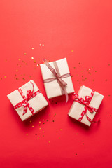 Creative composition with red present box, ribbons holiday decorations on red background