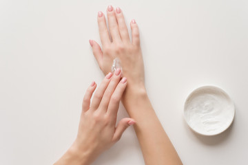 The girl distributes moisturizing cream on her hands. Hands on a white background with a jar of...