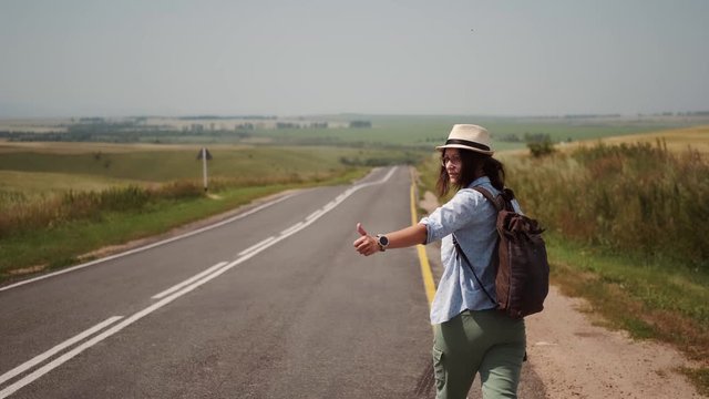 traveler hitchhiking by the side of the road. tourist with a backpack and a hat trying stop the car.