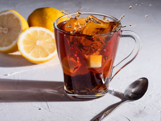 Cubes of sugar are falling from tea with lemons on the table.