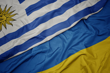 waving colorful flag of ukraine and national flag of uruguay.